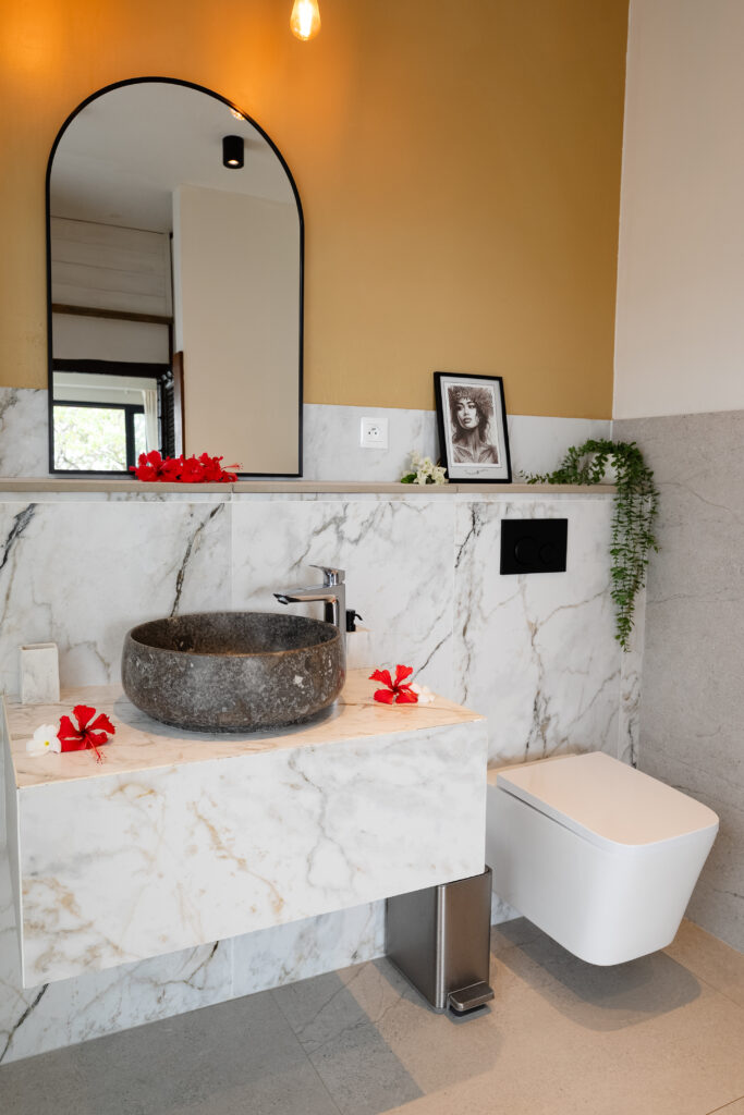 Elegant private bathroom featuring a stone basin, marble finishes and warm tropical decor.