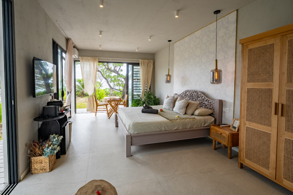 Spacious Oceanfront Hideaway Suite with king-size bed, wooden wardrobe and glass doors opening towards the seaside garden.
