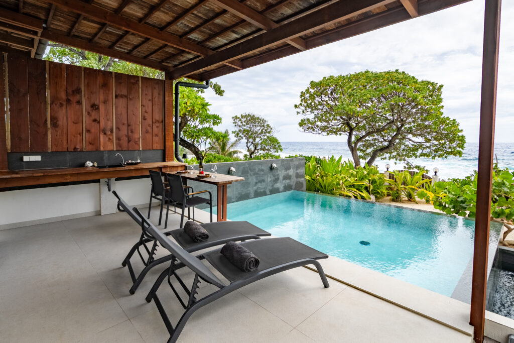 Covered terrace with two sun loungers beside a private infinity pool overlooking the Pacific Ocean.
